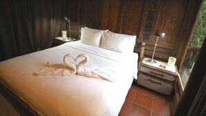 A neatly made bed with a towel swan, a bedside lamp, and a suitcase on a wooden nightstand.