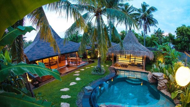 A resort with a swimming pool, thatched-roof structures, and lush greenery.