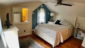 Un dormitorio con cama, cómoda, espejo, ventilador de techo y una mesita.