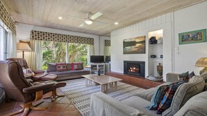 Una sala de estar acogedora con chimenea, asientos cómodos, televisión y un ventanal con cortinas.