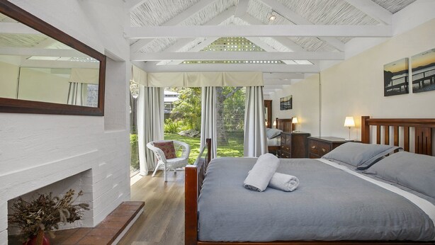 Un dormitorio con una cama grande, cabecera de madera, una mesita de noche, una silla y vistas a un jardín a través de un ventanal.