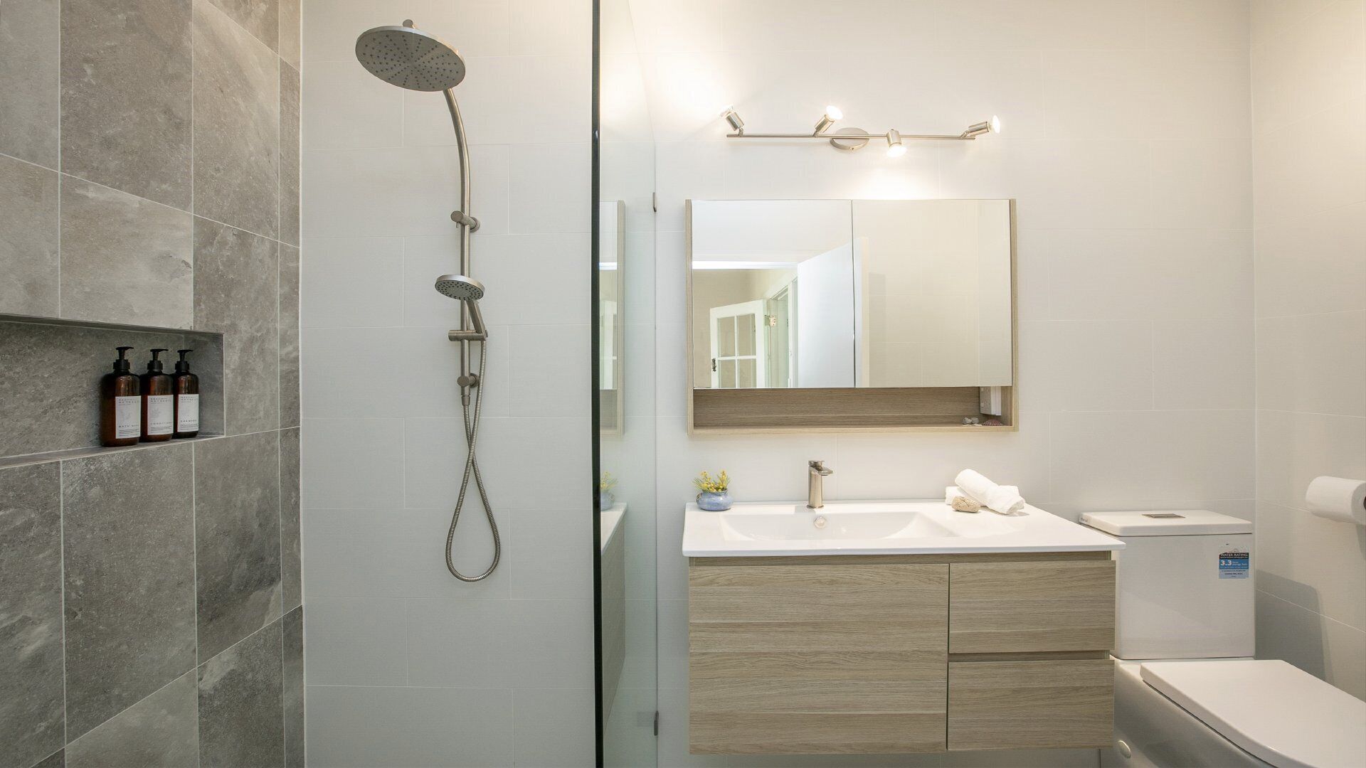 A modern bathroom with a shower, a sink with a mirror, and toiletries on a shelf.
