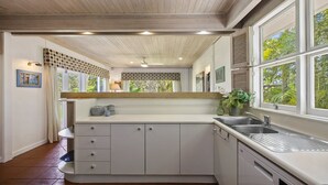 Una cocina moderna con armarios blancos, lavavajillas integrado y un ventanal con vistas a zonas verdes.