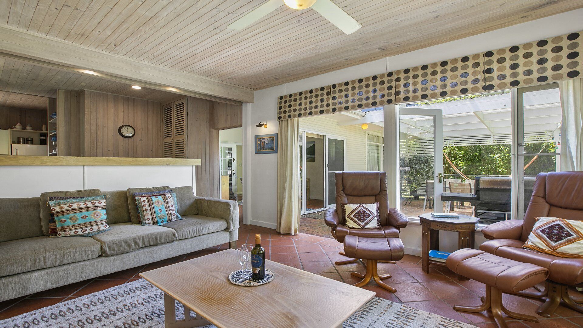 A cozy living room with a sofa, armchairs, and a coffee table. There is a sliding glass door leading to an outdoor area with a barbecue.
