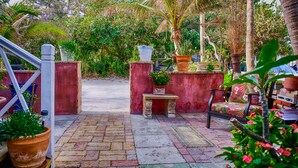 A garden pathway leading to a seating area with a bench and a table, surrounded by potted plants and a red wall. - Located steps from the ocean, offering true beach living (Hollywood)