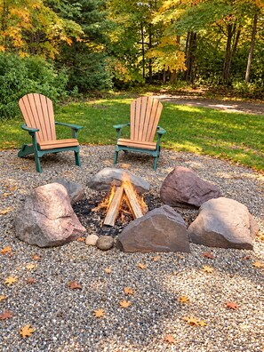 Zwei Adirondack-Stühle gegenüber, dazwischen eine Feuerstelle, umgeben von Kieselsteinen und Herbstlaub.