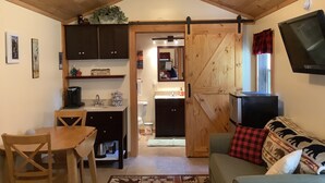 Ein gemütliches Interieur mit Holzbalkendecke, einem Essbereich, einer Couch mit gemusterten Kissen und einem an der Wand befestigten Fernseher.