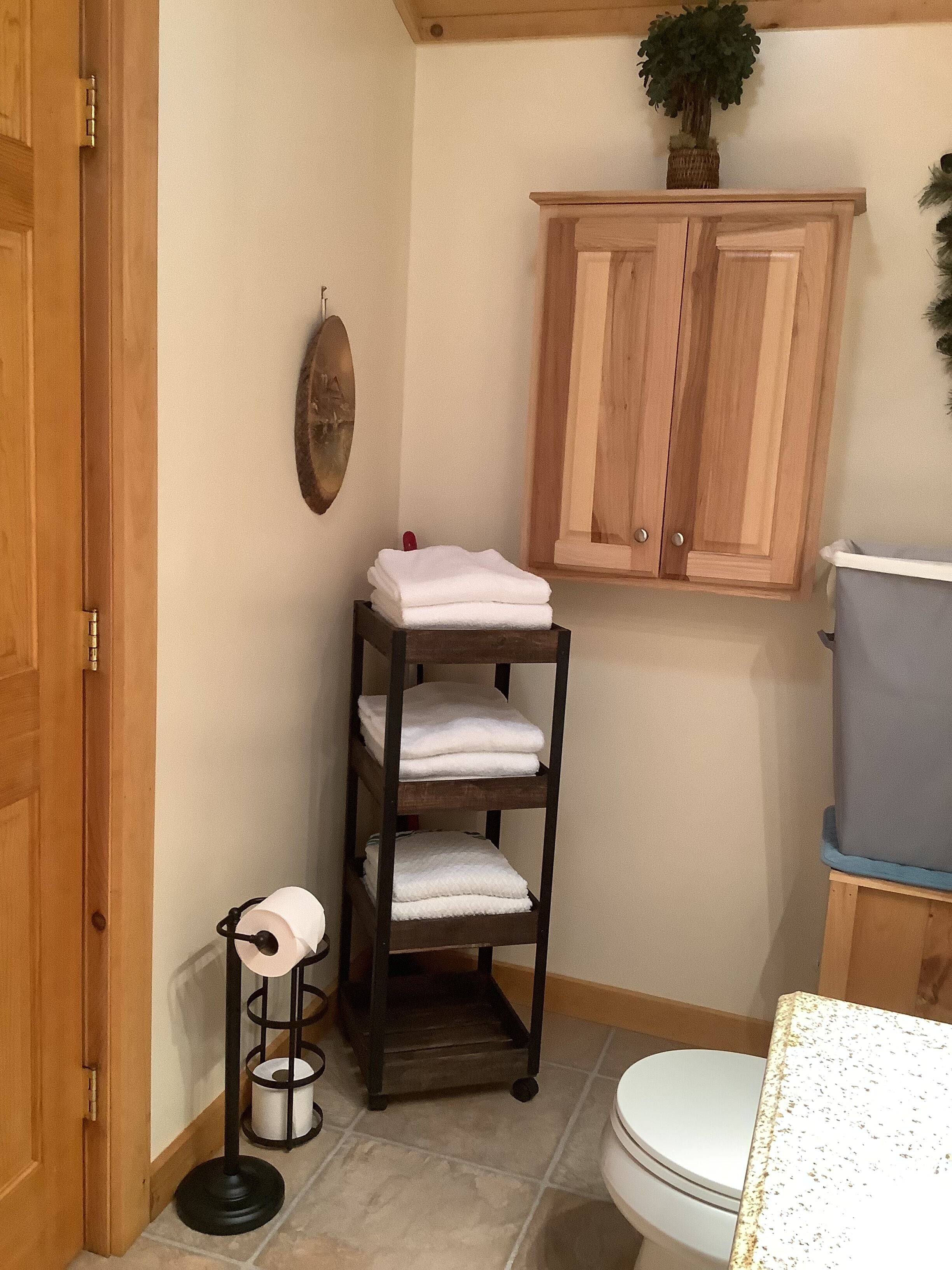 A bathroom with a wooden cabinet, a shelf with folded towels, a toilet, and a small plant on the wall.