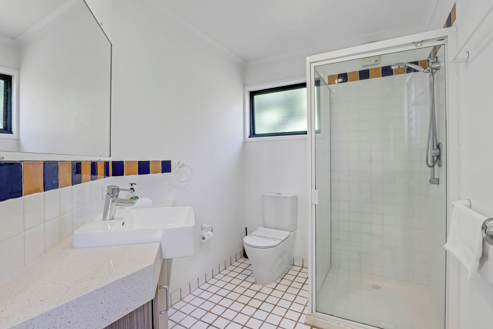 A bathroom with a shower, toilet, sink, and a window.