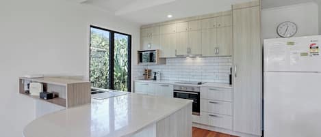 A modern kitchen with a central island, wooden cabinets, a built-in oven, and a refrigerator.