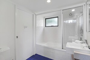 A modern bathroom with a glass-enclosed shower, a white bathtub, and a sink with a countertop. - Easy walk to Home and Cylinder Beaches (Point Lookout)
