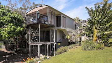 A two-story house with a balcony on the upper floor, surrounded by greenery and a well-maintained lawn.