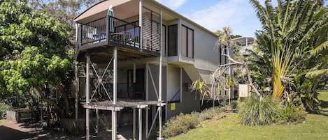 Una casa de dos pisos con un balcón en el nivel superior, rodeada de vegetación y un césped cuidado.