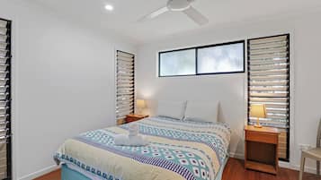 A bedroom with a bed, two bedside tables, a ceiling fan, and a window with blinds.