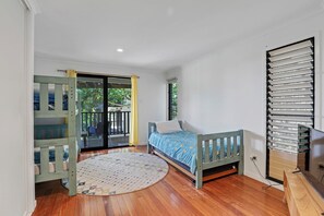 Une chambre à coucher avec un lit, une fenêtre avec des stores, un plancher en bois et un balcon avec une chaise.