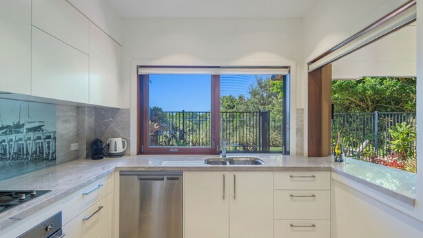 Eine moderne Küche mit Geschirrspüler, doppelter Spüle und Blick auf einen Garten durch große Fenster.