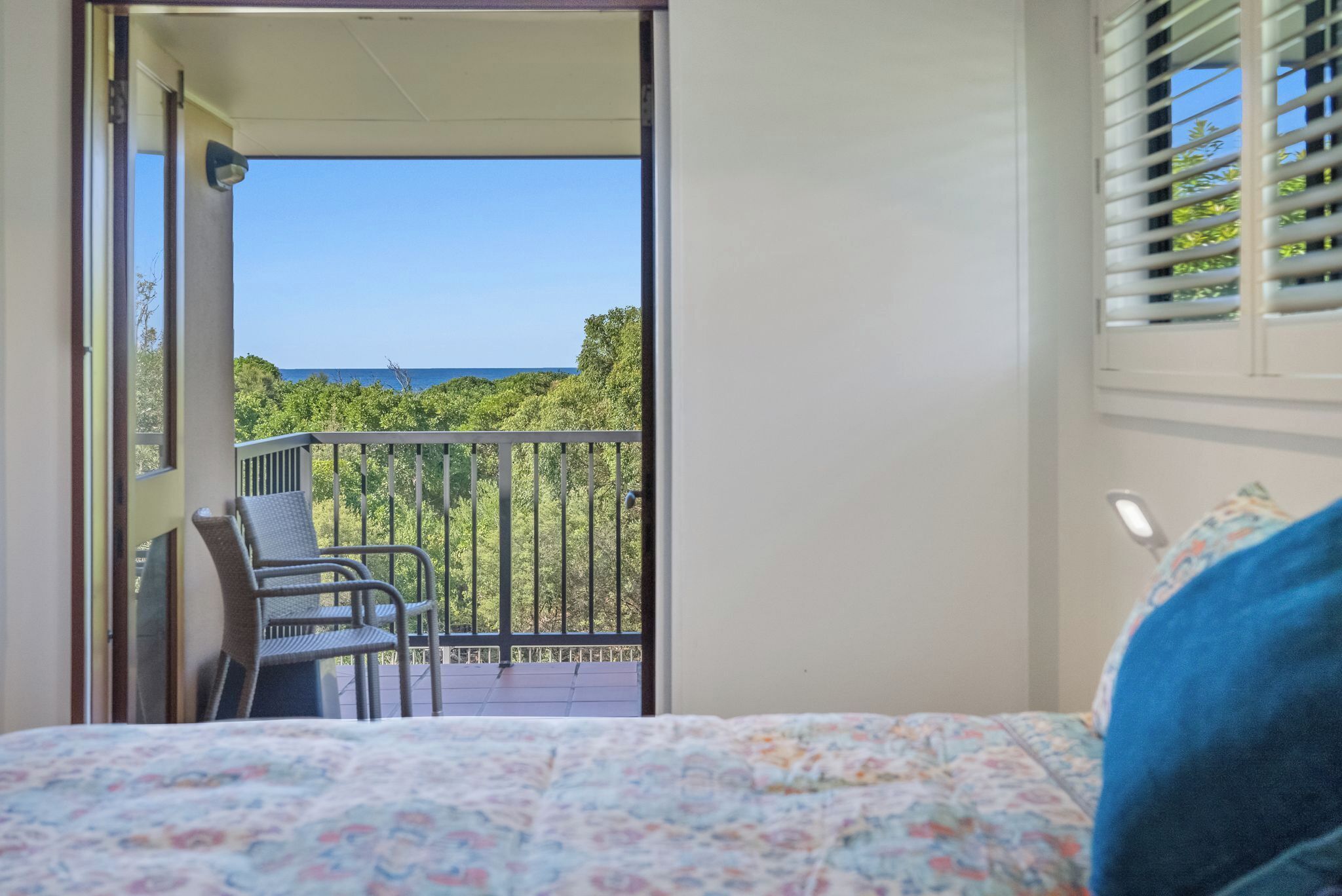 A bedroom with a bed, a chair, and a balcony with a view of the sea and trees.