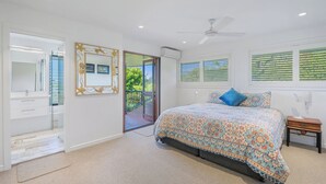 Ein Schlafzimmer mit einem großen Bett, einem Deckenventilator, einem Nachttisch und einem Fenster mit Jalousien.