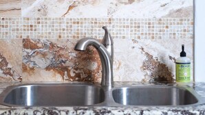 A kitchen with a marble backsplash, a stainless steel sink, and a bottle of hand soap. - Updated Quiet and Comfortable Uptown 1br Apt (New Orleans)