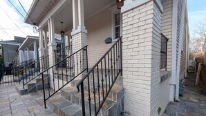 A two-story house with a stone staircase, white brick exterior, and a covered porch with columns. - Updated Quiet and Comfortable Uptown 1br Apt (New Orleans)