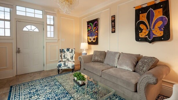 A living room with a beige sofa, patterned rug, decorative chair, and artwork on the walls. - Updated Quiet and Comfortable Uptown 1br Apt (New Orleans)