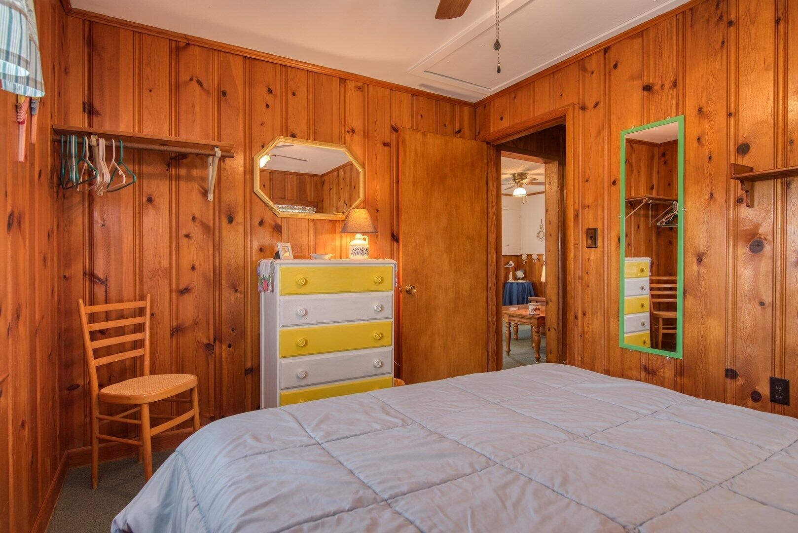 A wooden-paneled bedroom with a bed, a dresser, a chair, and a mirror.