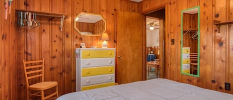A wooden-paneled bedroom with a bed, a dresser, a chair, and a mirror.