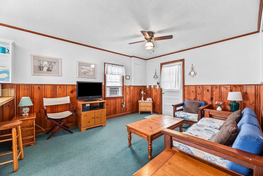 A cozy living room with wooden paneling, a ceiling fan, a television, a dining table, and a blue sofa.