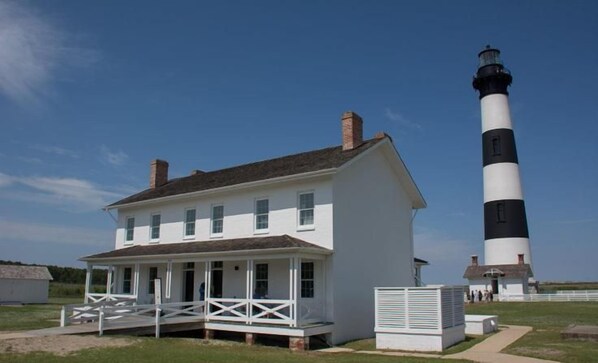 A white colonial-style house with a porch and a black and white lighthouse in the background.