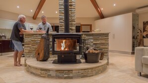 A modern kitchen with a stone fireplace, a wooden barrel, and a metal bucket filled with firewood. - Almonta Park Lodge (Coffin Bay)