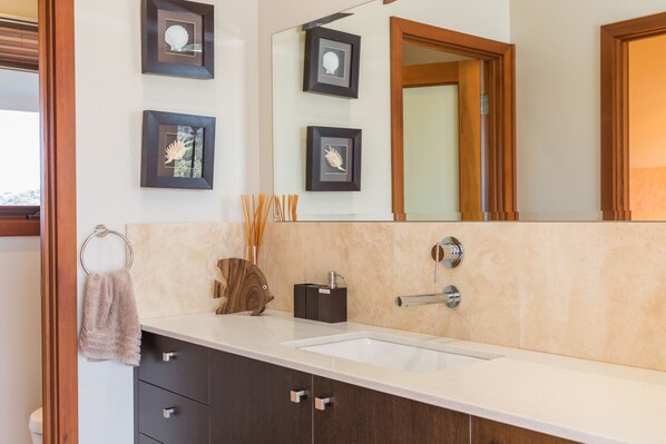 A modern bathroom with a large sink, dark wooden cabinets, and framed artwork on the wall.