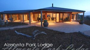 A modern lodge with a covered patio area, large potted plants, and a well-lit entrance. - Almonta Park Lodge (Coffin Bay)