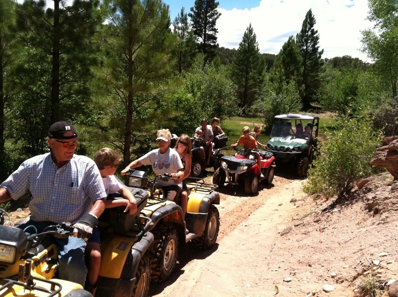 A group of people riding ATVs on a dirt path surrounded by trees.