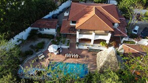 Luftaufnahme eines Hauses mit Swimmingpool, Terrasse und Gartenmöbeln sowie einem großen Felsen.