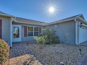 A residential house with a brick pathway leading to the front door, a small garden with pebbles, and a clear sky.