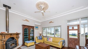 A living room with a fireplace, a yellow sofa, a wooden coffee table, and a ceiling fan. - Doc's Cottage Lancelin - Ocean Views - Pet Friendly. (Lancelin)