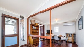 A spacious room with a wooden floor, a dining area with a table and chairs, a bookshelf, and a television. - Doc's Cottage Lancelin - Ocean Views - Pet Friendly. (Lancelin)