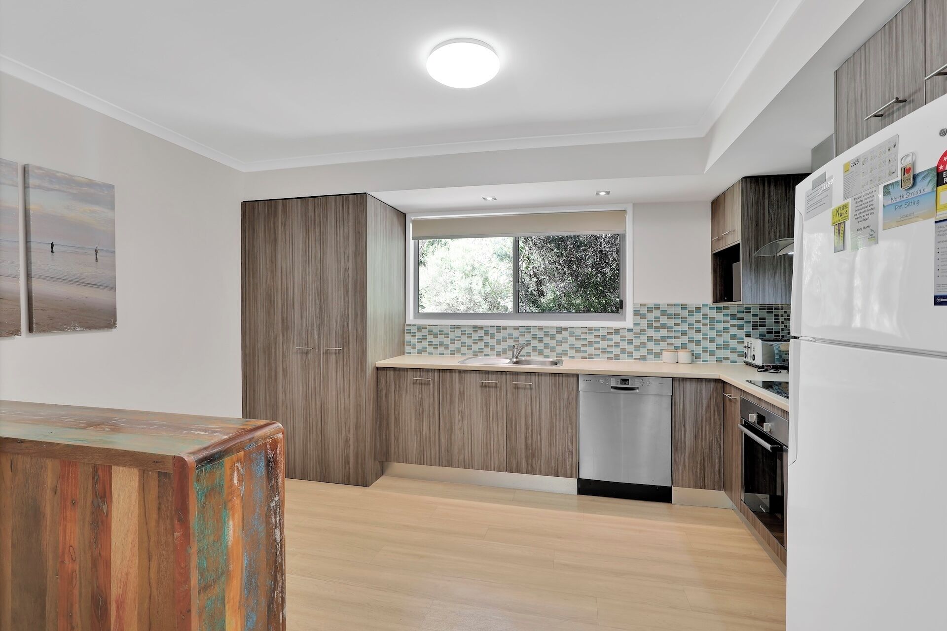 Une cuisine moderne avec des meubles en bois, un lave-vaisselle encastré et une fenêtre laissant entrer la lumière naturelle.