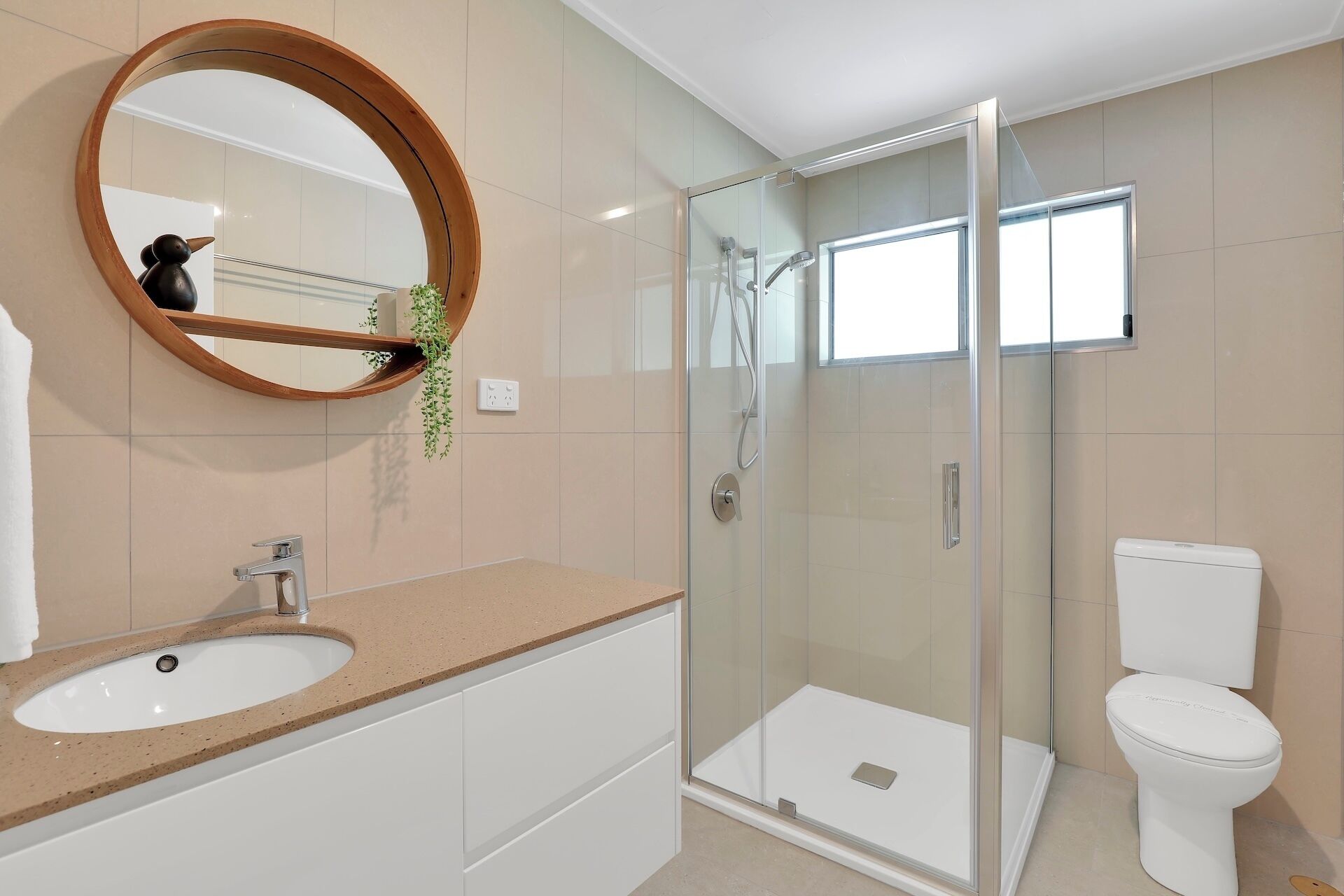 A modern bathroom with a glass-enclosed shower, a white toilet, and a beige countertop with a sink.