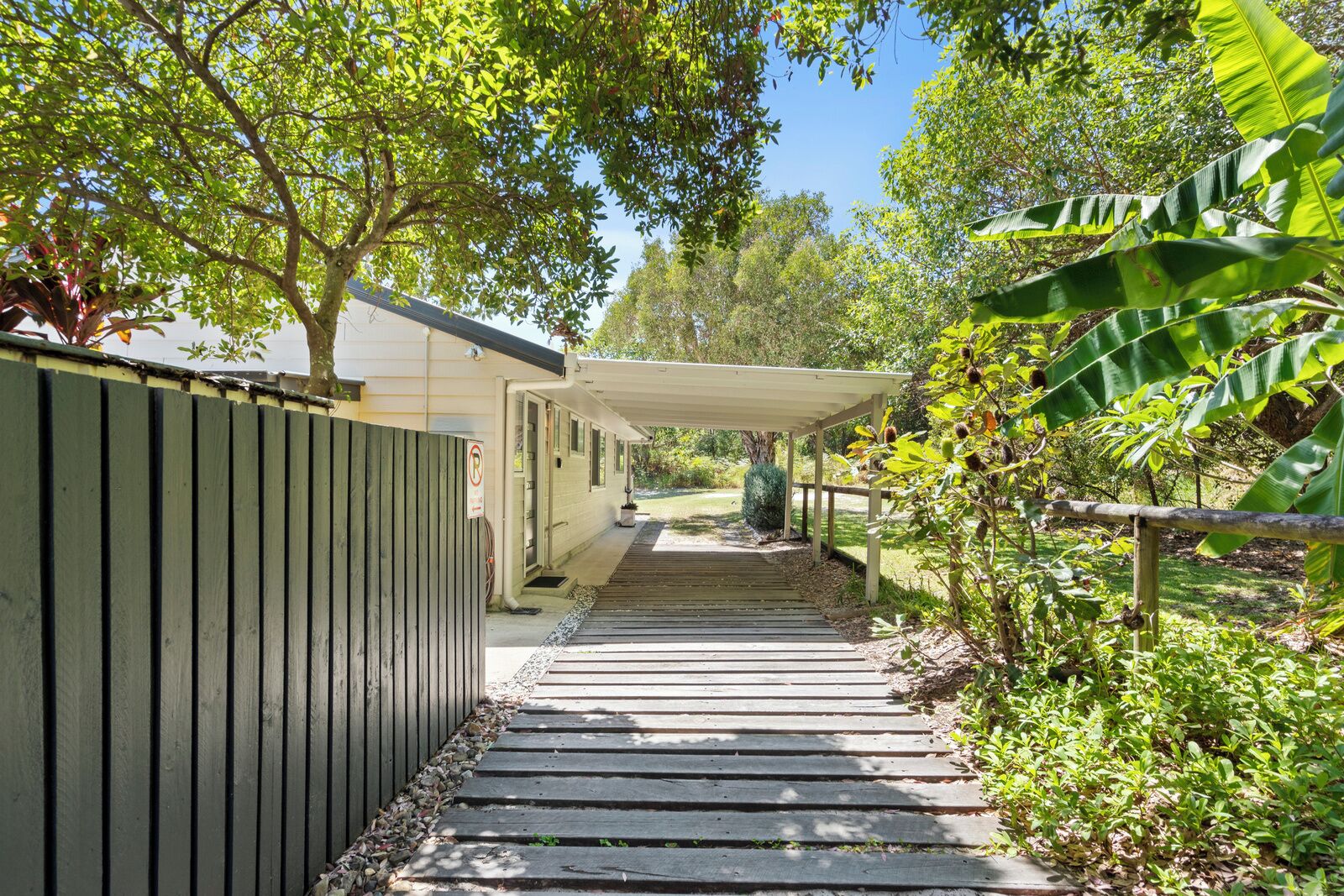 A covered walkway leading to a building with a 'No Parking' sign, surrounded by lush greenery and trees.