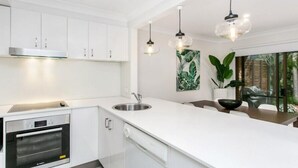 Una cucina moderna con mobili bianchi, forno integrato, lavello in acciaio inossidabile e luci a sospensione.