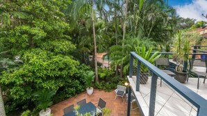 Un giardino pensile con vegetazione rigogliosa, un'area salotto con tavoli e sedie, e vista sugli alberi circostanti.