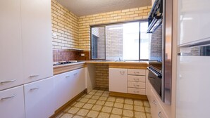 Une cuisine compacte avec des meubles blancs, un pare-feu en carrelage et une fenêtre qui laisse entrer la lumière naturelle.