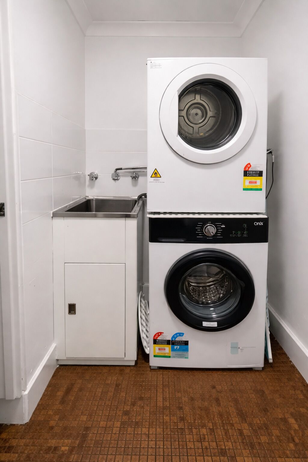 A laundry room with a stacked washer and dryer, a sink, and a cabinet.