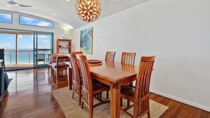 A spacious dining area with a wooden table and chairs, a large window offering a view of the ocean, and a ceiling fan. - Panoramic ocean and beach views from this beautifully appointed two... (Point Lookout)