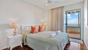 A bedroom with a bed, two bedside tables, a ceiling fan, and a view of the ocean through a sliding door. - Panoramic ocean and beach views from this beautifully appointed two... (Point Lookout)