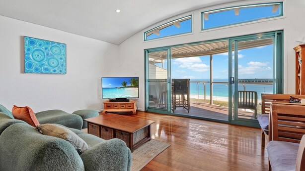 A spacious living room with a large TV, comfortable seating, and a sliding glass door leading to a balcony with a view of the ocean. - Panoramic ocean and beach views from this beautifully appointed two... (Point Lookout)