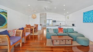 A modern living room with a wooden dining table, a green sofa, and a kitchen in the background. - Panoramic ocean and beach views from this beautifully appointed two... (Point Lookout)