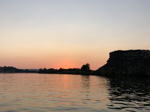 Een kalm wateroppervlak weerspiegelt een zonsondergang, met een rotsachtige klif aan de rechterkant.