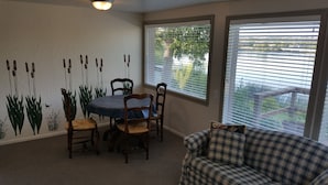 A dining area with a round table, four chairs, and a wall mural of tall grasses. There is a window with blinds and a view of greenery outside. - Amazing relaxing get-away home on the Snake River with river view and boat dock. (Hagerman)